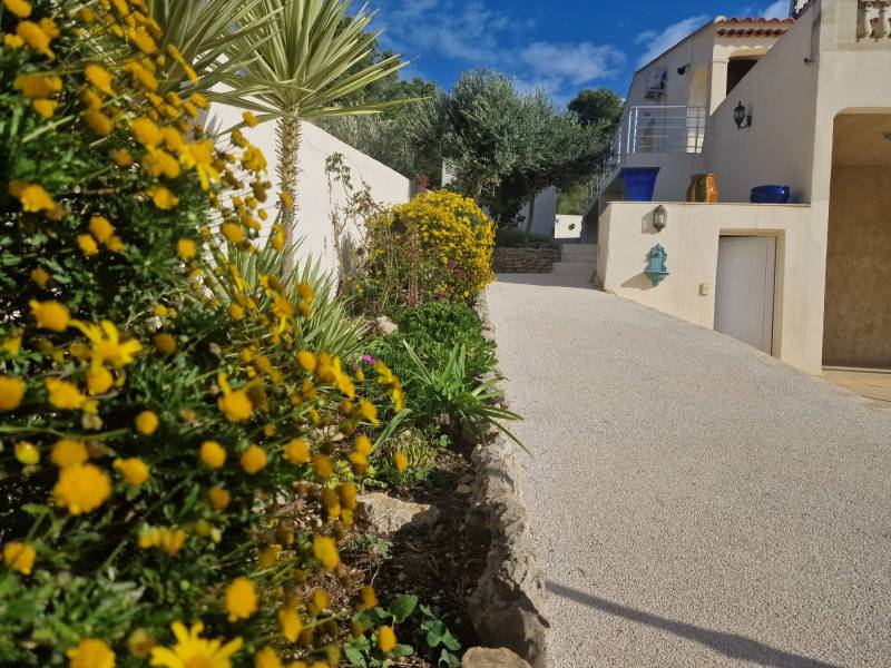 Photo de l'aménagement d'un allée carrosable au bordure fleuri au teinte jaune pour une maison de vacance estival agréable avec un extérieur luxuriant grâce a notre allée carrossable en MIneralstar, notre résine drainte et naturel respectueuse de l'enviro